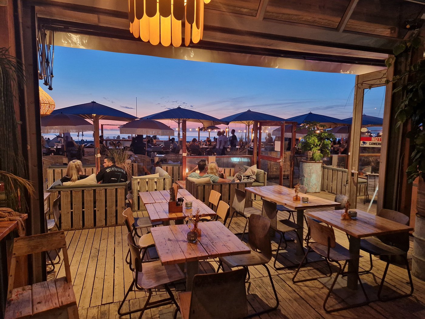 Avondsfeer op het strandterras van beachclub Solbeach Scheveningen met verlichte tafels.