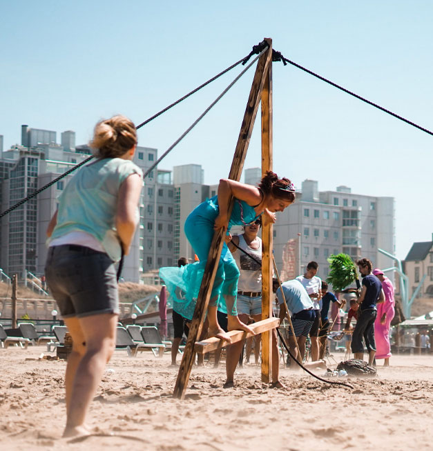 Deelnemers bouwen aan een houten constructie tijdens Expeditie Robinsol bij beachclub Solbeach.