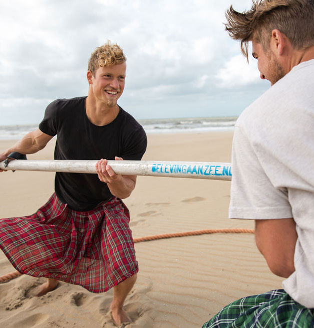 Krachtmeting en paalwerpen tijdens de Highland Games teambuilding op het strand van Scheveningen.