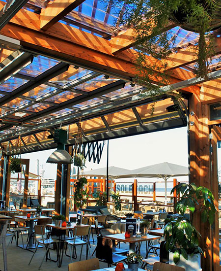 Zonovergoten terras met pergola en loungeplekken bij strandtent Solbeach Scheveningen.