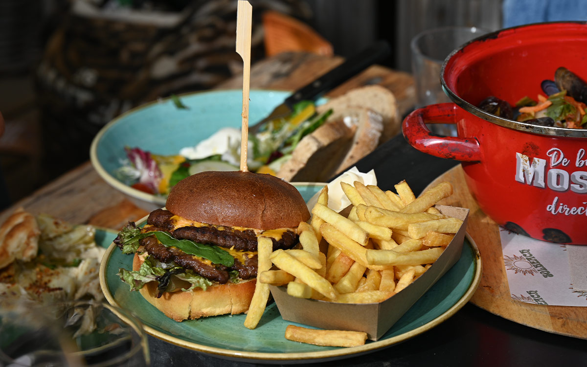 Luxe burger met frites geserveerd op een houten plank bij beachclub Solbeach.