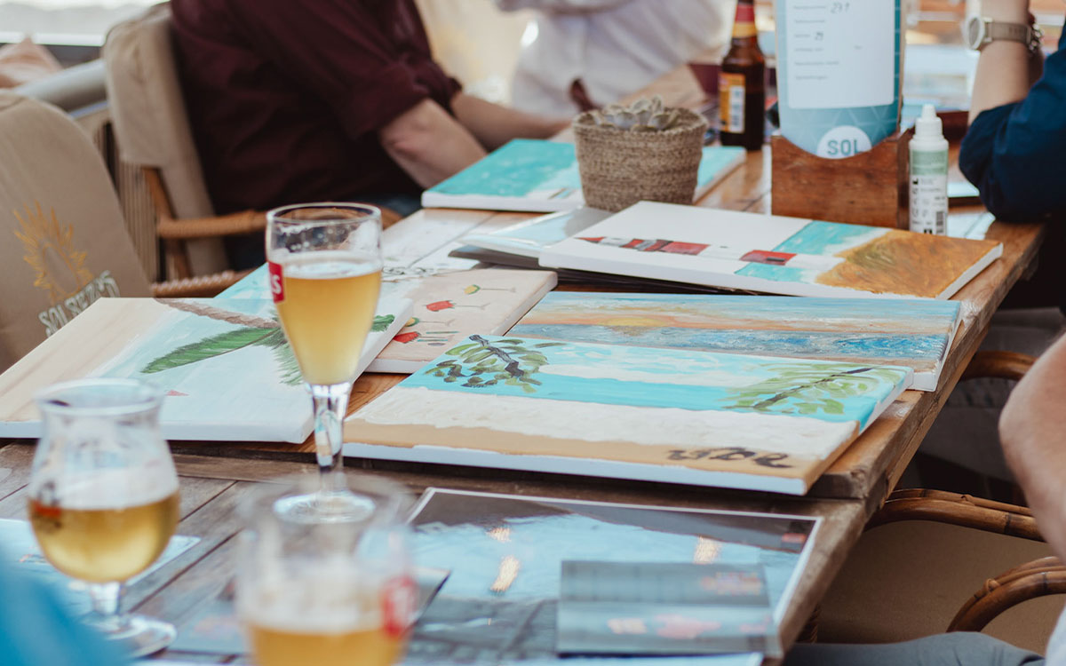 Schilderworkshop aan tafel op het terras van beachclub Solbeach als teambuilding uitje.