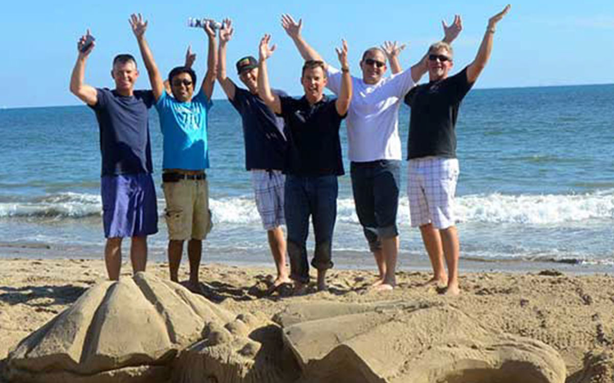 Juichend team bij hun zelfgemaakte zandsculptuur tijdens een bedrijfsuitje in Scheveningen.