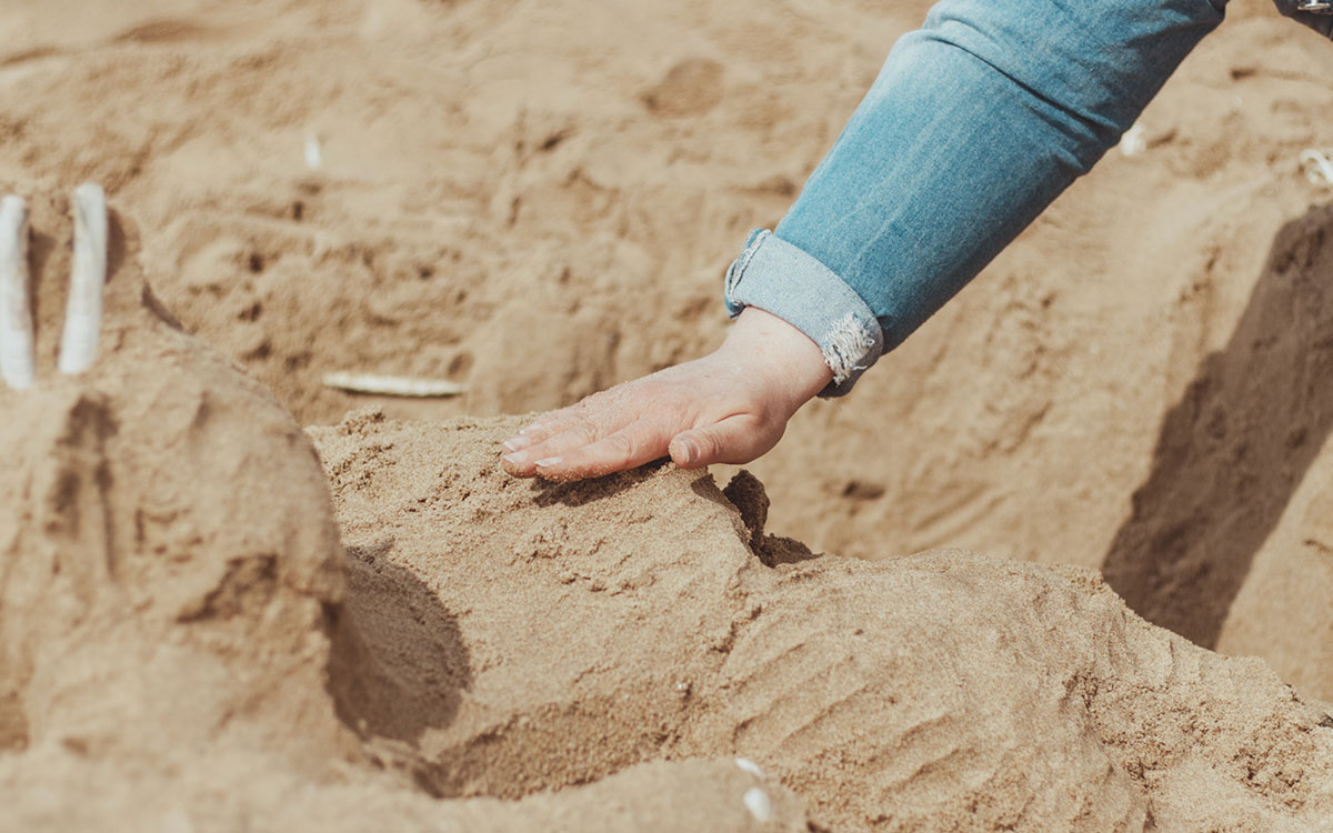 Deelnemers bouwen aan zandsculpturen tijdens een teambuilding activiteit op het strand.