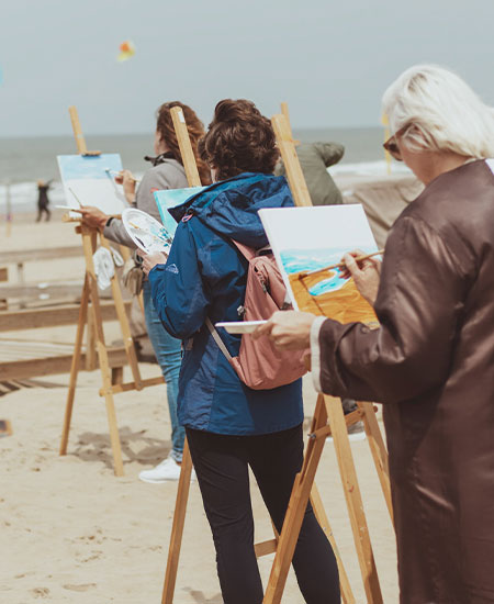Workshop schilderen aan zee met schildersezels en uitzicht op het strand van Scheveningen.