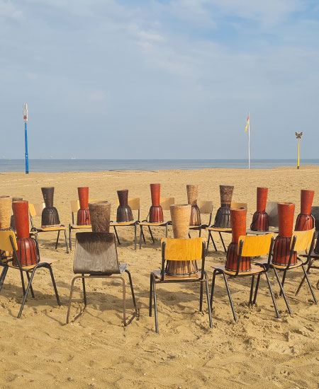 Cirkel van djembé trommels op het strand van Scheveningen voor een muzikale teambuilding.