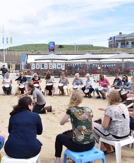 Grote groep collega's vormt een percussiecirkel op het strand voor beachclub Solbeach.