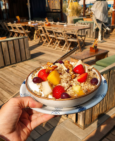 Gezond ontbijt met yoghurt en granola met uitzicht op het rustige strandterras van Solbeach.