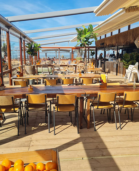 Feestelijke zaalinrichting met lange houten biertafels voor groepen bij strandtent Solbeach.