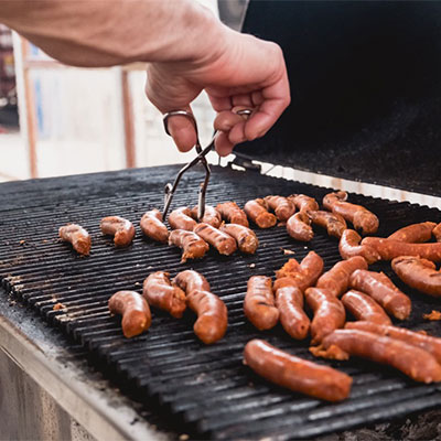 Worstjes sissen op de grill tijdens een gezellige strandbarbecue bij Solbeach Scheveningen.