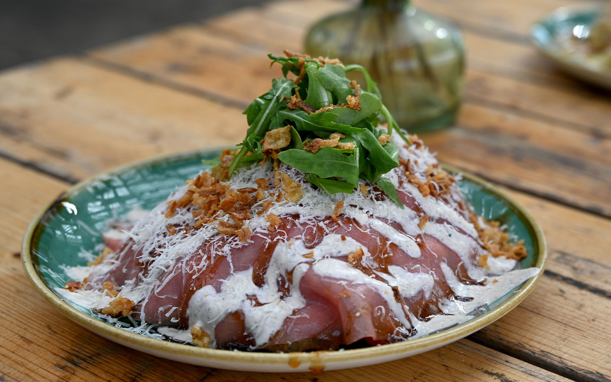 Rijk opgemaakte carpaccioschotel met rucola en dressing bij beachclub Solbeach Scheveningen.