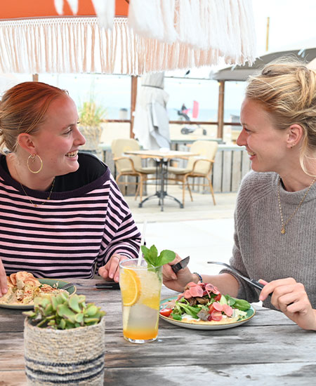 Collega's ontspannen en kletsen tijdens een zakelijke lunch op het terras van Solbeach Scheveningen.
