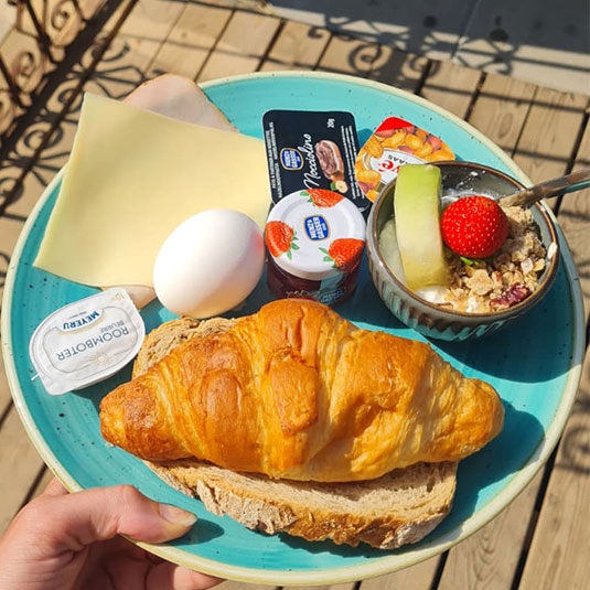 Uitgebreid ontbijtbord met croissant, gekookt ei en vers fruit bij beachclub Solbeach Scheveningen.
