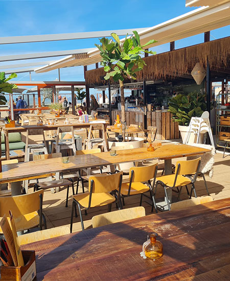 Terrasopstelling met houten tafels en uitzicht op de Noordzee bij strandtent Solbeach.
