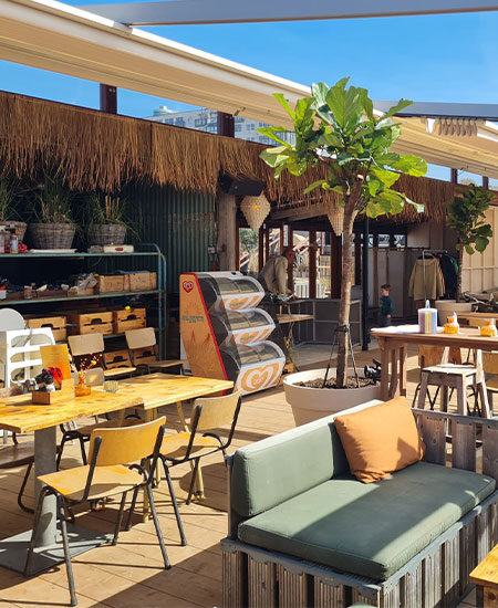 Loungegedeelte met rotan meubels en tropische planten bij beachclub Solbeach.