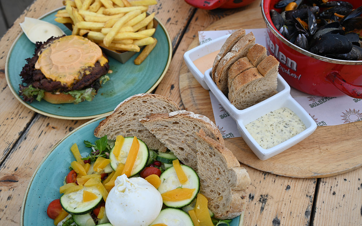 Diverse dinergerechten waaronder burgers, friet en salades bij strandtent Solbeach.