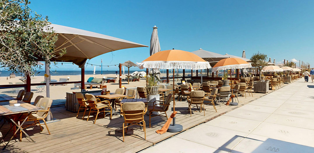 Zonovergoten terras met parasols en loungebanken bij beachclub Solbeach in Scheveningen.